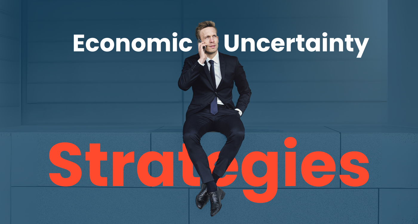 Businessman in a suit sitting on blue blocks, thinking on a phone call, with the words “Economic Uncertainty Strategies” in bold text.
